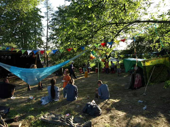 Festivalgäste sitzen zwischen Hängematten und Bäumen auf dem Gelände.