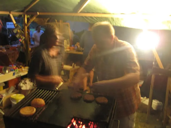 Zwei Personen bereiten Essen am offenen Grill zu.