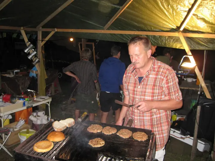Ein Helfer grillt Burger unter einem Zeltdach.