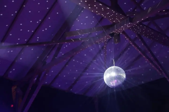 Eine Discokugel hängt unter einem violett beleuchteten Zeltdach.