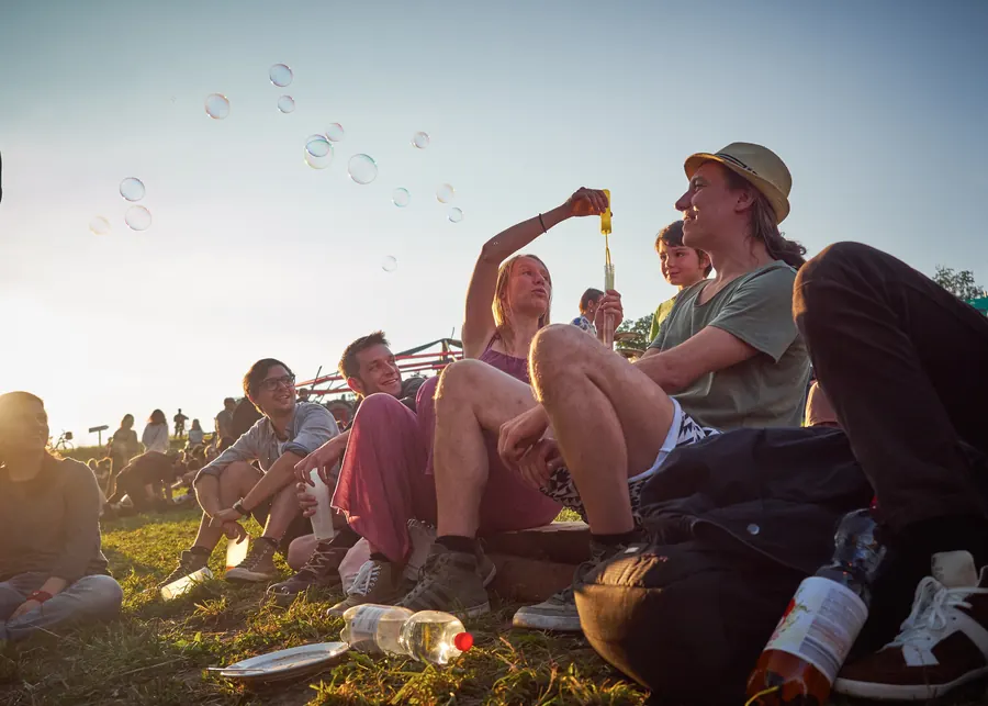 Festivalgäste sitzen bei Abendsonne gemeinsam auf der Wiese.