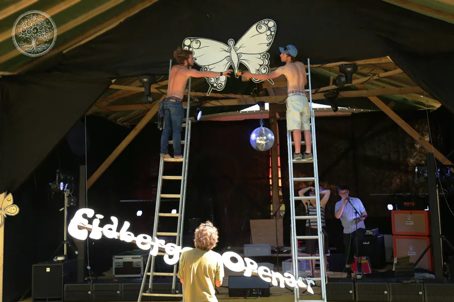 Freiwillige befestigen eine grosse Schmetterlingsdekoration über der Bühne.