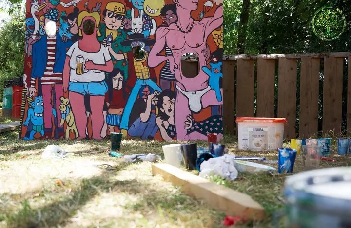 Eine bemalte Figurenwand und Arbeitsmaterial stehen auf dem Festivalgelände.