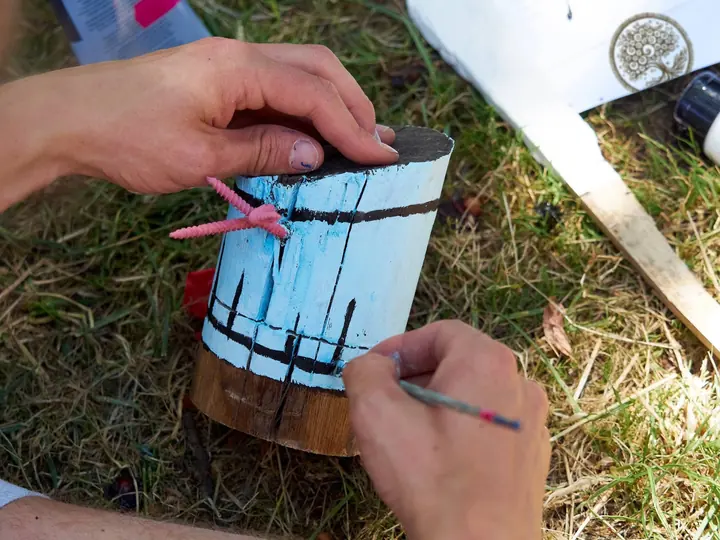Eine Hand malt blaue Streifen auf ein kleines Holzstück.